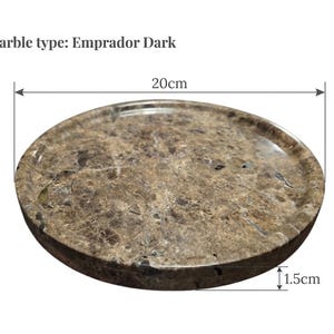 Puede incluir: Una bandeja redonda de m&aacute;rmol Emperador Dark, de 20 cm de di&aacute;metro y 1,5 cm de grosor. La bandeja es de color marr&oacute;n oscuro con vetas m&aacute;s claras. El texto "Marble type: Emprador Dark" es visible.
