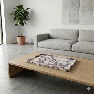 May include: A rectangular marble tray with a white and purple veined pattern rests on a light wood coffee table. The tray is the focal point of a modern living room setting, with a grey sofa and potted plant in the background.