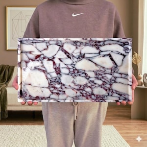 May include: Rectangular tray with a polished surface. The tray features a striking pattern of white and deep purple marble-like veining. The tray is held up by a person. The tray is a decorative item.