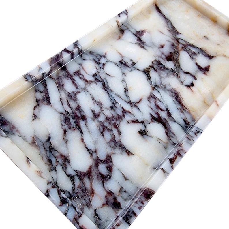May include: Rectangular marble tray with a white base and dark purple veining. The tray has a raised edge and a polished finish. The marble pattern is unique, with a mix of colors and textures. This tray is suitable for serving or display.