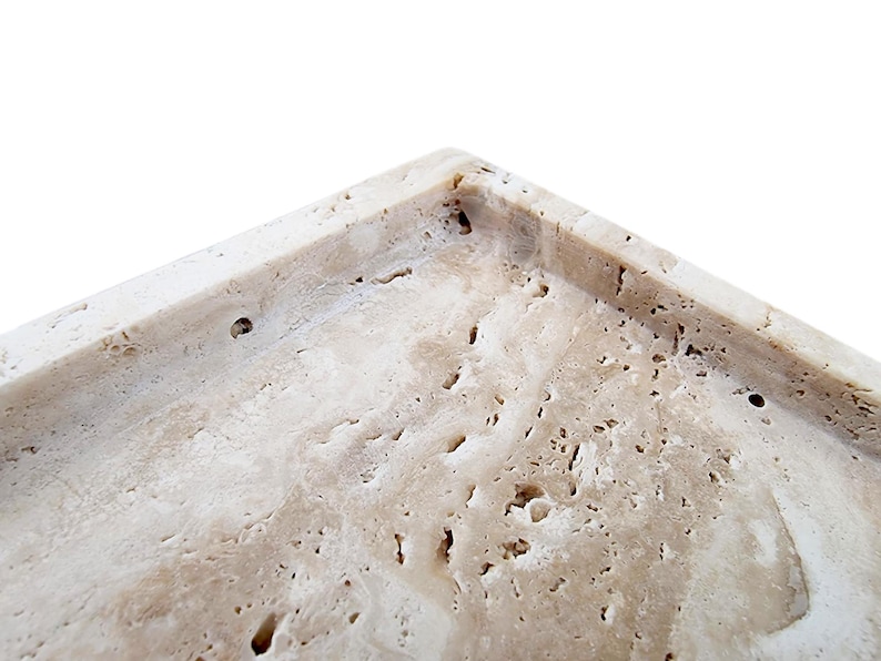 May include: Close-up of a rectangular, beige-colored tray with a textured surface. The tray has a porous, stone-like appearance with small holes and variations in color. The corner of the tray is visible against a white background.