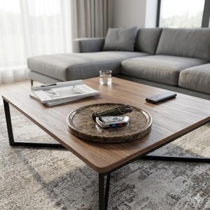 Puede incluir: Una escena de sal&oacute;n moderno con una mesa de centro de madera oscura y un marco de metal negro. Una bandeja decorativa contiene una llave de coche y un mando a distancia. Tambi&eacute;n se ve un sof&aacute; gris y un vaso de agua.