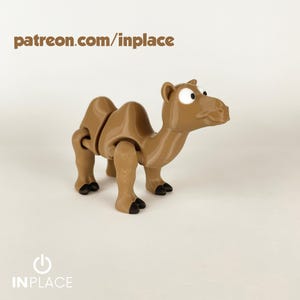 Puede incluir: Un juguete de camello articulado marrón con pezuñas negras y ojos grandes de dibujos animados. El texto "patreon.com/inplace" está impreso encima del camello. El logotipo "INPLACE" está impreso debajo.