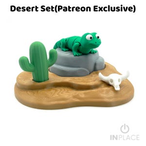 May include: A Desert Set (Patreon Exclusive) featuring a green lizard figurine resting on a grey rock, a green cactus, and a white animal skull on a tan base with a wood grain texture. The set includes a green lizard, a grey rock, a cactus, and a skull.