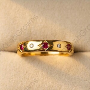 Peut inclure: Une bague en or ornée de trois pierres rouges et de deux petites pierres transparentes. La bague est présentée dans un écrin en bois avec un intérieur beige clair. Le design de la bague présente un motif répétitif de pierres précieuses.