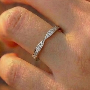 May include: A silver-toned metal ring featuring a delicate twisted band design. The surface of the band is embedded with a series of small, clear, sparkling stones that follow the curve of the metal, creating a continuous line of light reflection.
