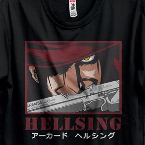Può includere: T-shirt nera con grafica dell'anime Hellsing. Il design presenta un personaggio con una pistola, la scritta "HELLSING" e testo giapponese. La t-shirt è appesa a una gruccia nera.