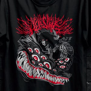 Può includere: T-shirt nero con una grafica dettagliata di un mostro con molteplici occhi e una grande bocca, con accenti rossi e bianchi. La maglietta è appesa a una gruccia nera contro un muro di mattoni scuri. Il logo Stitch Aura è visibile.