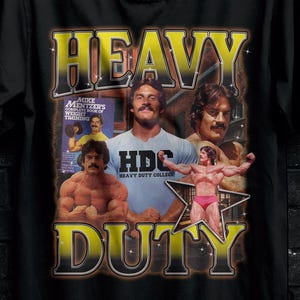 May include: Black t-shirt with a graphic featuring the text "HEAVY DUTY" in yellow, along with images of bodybuilders. The shirt also has the text "HDC Heavy Duty College".