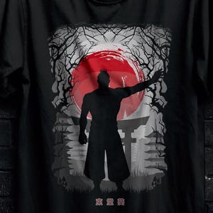 May include: Black t-shirt featuring a silhouette of a person with an outstretched arm in front of a red sun and Japanese-style architecture. The shirt is hanging on a black hanger.