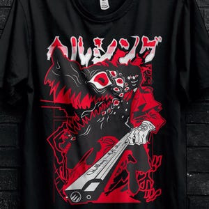Può includere: T-shirt nero con un design grafico rosso e nero e testo giapponese. Il design presenta un personaggio con un'arma. La maglietta è appesa a una gruccia nera.