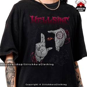 May include: Black t-shirt with the word "HELLSING" in dark red gothic lettering. The graphic shows two hands framing an eye with a red pupil and a star tattoo on one hand. The shirt has the text "etsy.com/shop/StitchAuraClothing" and "Copyright © StitchAuraClothing".