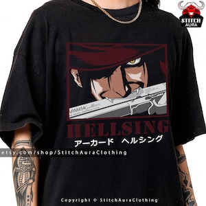 May include: Black t-shirt featuring a graphic of a character from the anime series Hellsing. The design includes the character's face, a gun, and the word "HELLSING" in red. The shirt also has Japanese text and the Etsy shop name.
