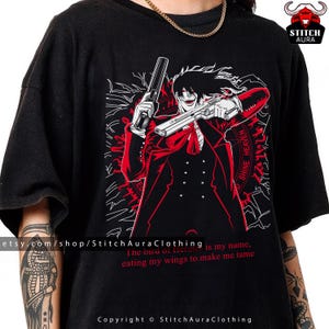 May include: Black t-shirt featuring a red and white graphic of an anime character holding two guns. The character is wearing a red suit and has long black hair. Text on the shirt includes "SHINE HEAVEN" and a quote.