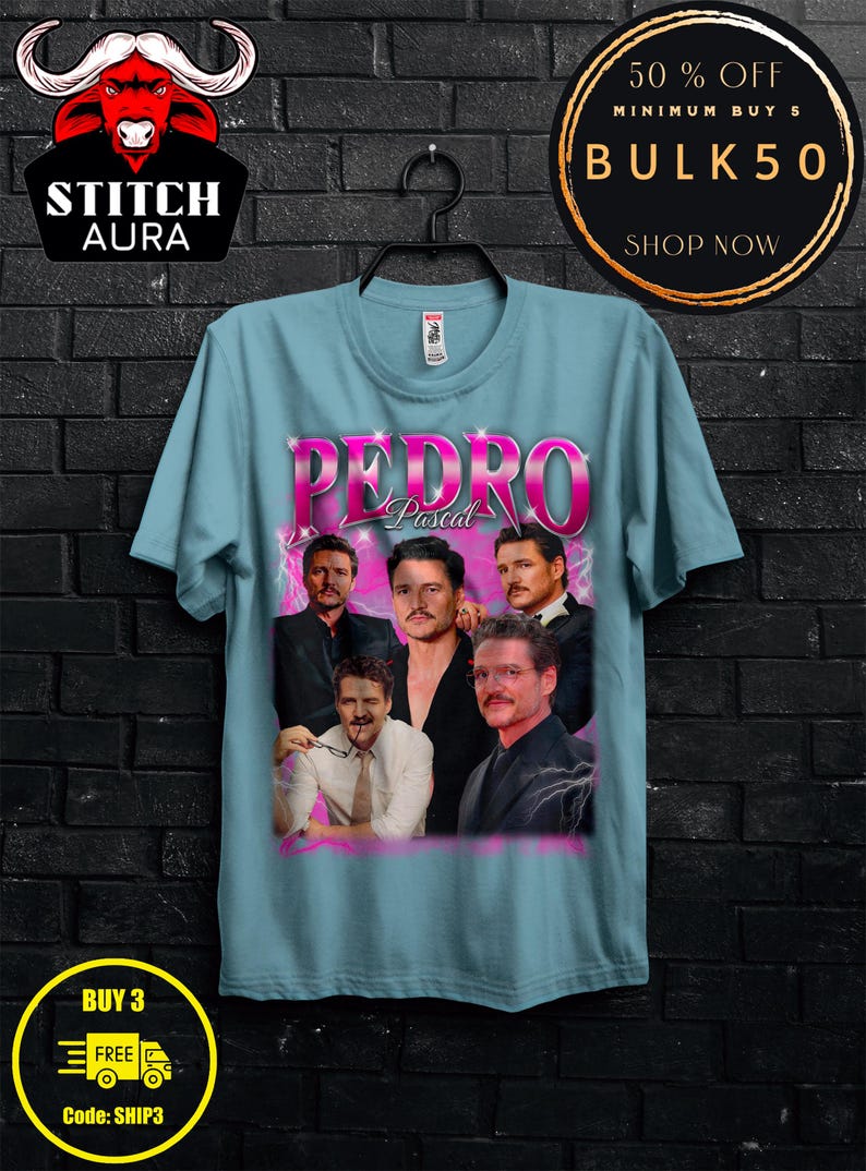 May include: Light blue t-shirt featuring a graphic of Pedro Pascal with the name "Pedro Pascal" in pink. The shirt has a crew neck and short sleeves. The image includes the "STITCH AURA" logo and promotional text.