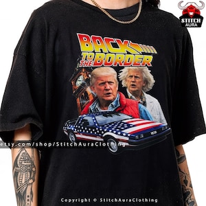 Könnte beinhalten: Schwarzes T-Shirt mit einem Aufdruck "BACK TO THE BORDER" in Gelb und Rot. Das Design zeigt Bilder von zwei Männern und einem Auto mit amerikanischem Flaggen-Design. Das Shirt hat einen Rundhalsausschnitt.