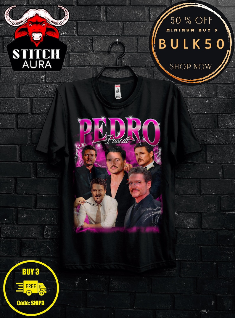 May include: Black t-shirt featuring a collage of images of Pedro Pascal with the name "PEDRO" in large, pink letters. The shirt also has the text "Pascal" below the name. The shirt is hanging on a black hanger.