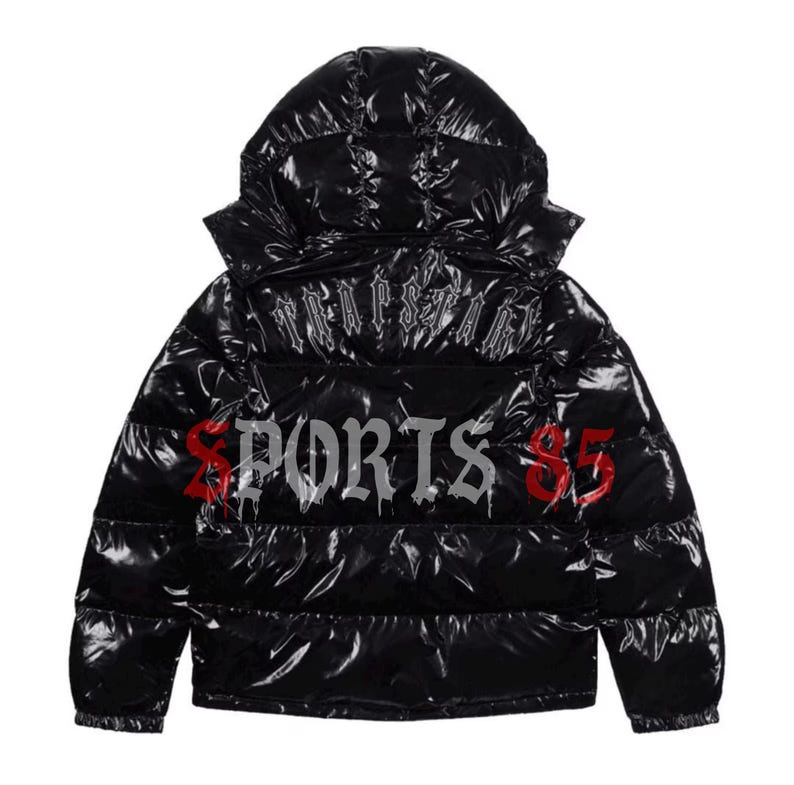 Pode incluir: Casaco puffer preto com capuz. O casaco tem a palavra "TRAPSTAR" nas costas e "SPORTS $5" em fonte g&oacute;tica. O casaco &eacute; brilhante e tem um design acolchoado.