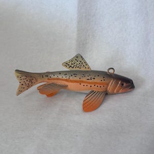 May include: A detailed, hand-painted fish ornament with a brown head, orange belly, and gray back. The fish has black spots and orange fins. A small metal loop is attached for hanging. This decorative item is perfect for fishing enthusiasts.