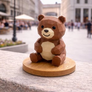 May include: A brown geometric bear figurine with a cream belly sits on a round wooden base. The bear has a smiling face and is made of triangular shapes. The background is blurred, showing a city street.