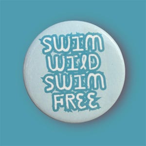 May include: A circular, pale blue badge featuring the words "SWIM WILD SWIM FREE" in a turquoise font. The badge has a slightly textured surface and a turquoise background.