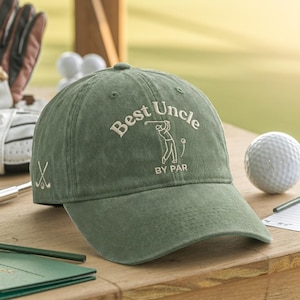 May include: Olive green baseball cap with the text "Best Uncle BY PAR" embroidered in white. The cap features a golf-themed design with a golfer graphic and crossed golf clubs on the side. A golf ball and other golf accessories are in the background.