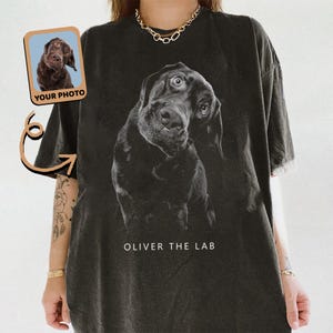 May include: Black t-shirt featuring a grayscale image of a Labrador Retriever with an inquisitive expression. The text "OLIVER THE LAB" is printed below the dog. A small image of a dog with the text "YOUR PHOTO" is in the upper left corner.
