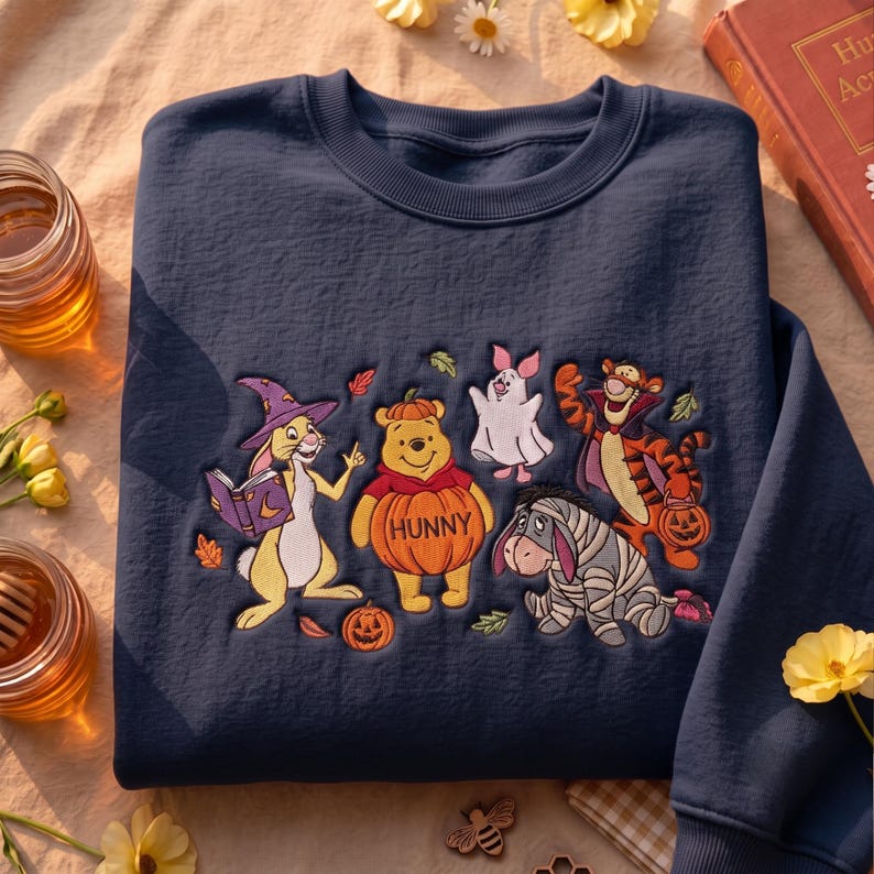 May include: A navy blue crewneck sweatshirt featuring an embroidered design of Winnie the Pooh characters dressed in Halloween costumes, including Rabbit as a wizard, Pooh as a pumpkin, Piglet as a ghost, Tigger as a vampire, and Eeyore as a mummy.