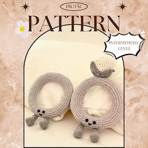 May include: Two grey crocheted baby toys, ring-shaped with small legs and smiling faces. One has a small crocheted ball on top. The image includes the text "DIGITAL PATTERN" and "INTERMEDIATE LEVEL".