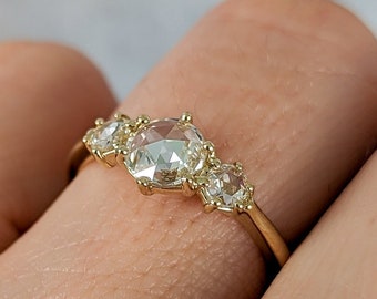 May include: A gold band ring with five round, clear gemstones. The ring is on a person's finger.