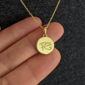 May include: Gold necklace with a round pendant featuring the Eye of Horus symbol.