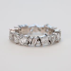 May include: A silver band ring with a row of various sized diamonds set in a staggered pattern.