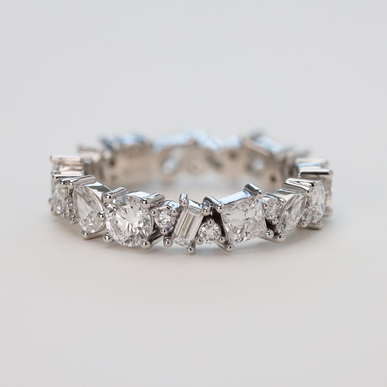 May include: A silver band ring with a row of various sized diamonds set in a staggered pattern.
