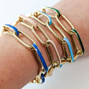 Peut inclure: Un ensemble de bracelets en cha&icirc;ne dor&eacute;e avec des accents d'&eacute;mail color&eacute;s. Les bracelets sont superpos&eacute;s sur le poignet d'une personne et pr&eacute;sentent des accents d'&eacute;mail bleu, rose et vert.