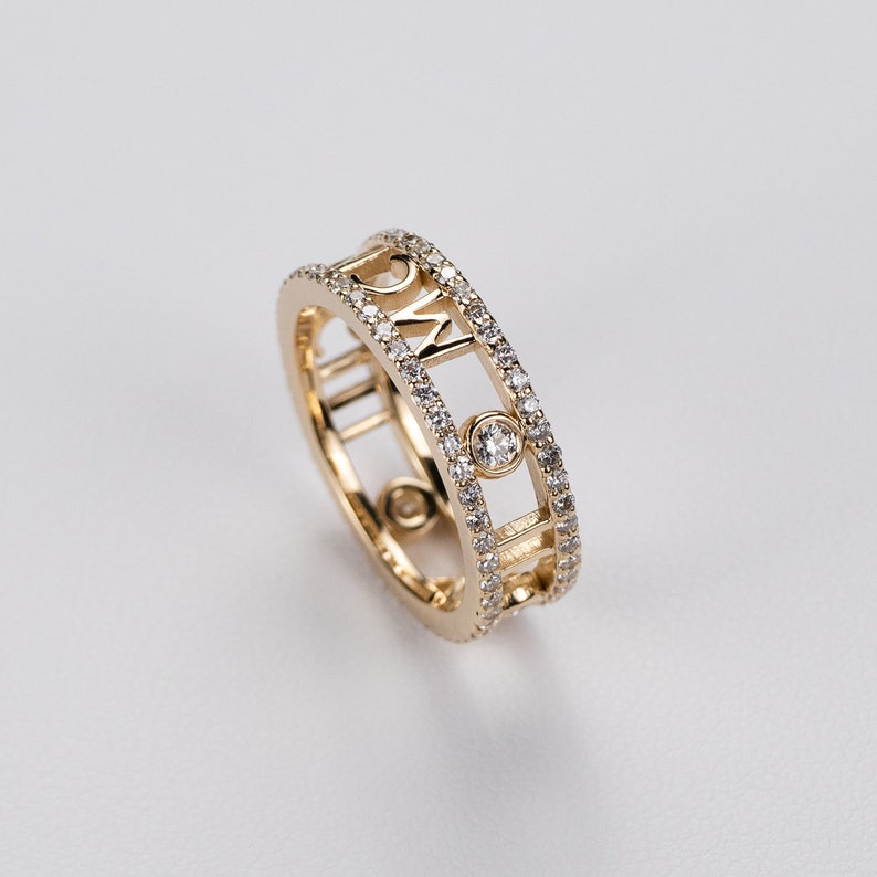 May include: A gold ring with a diamond-encrusted band and a cutout design featuring the letters "MCM".