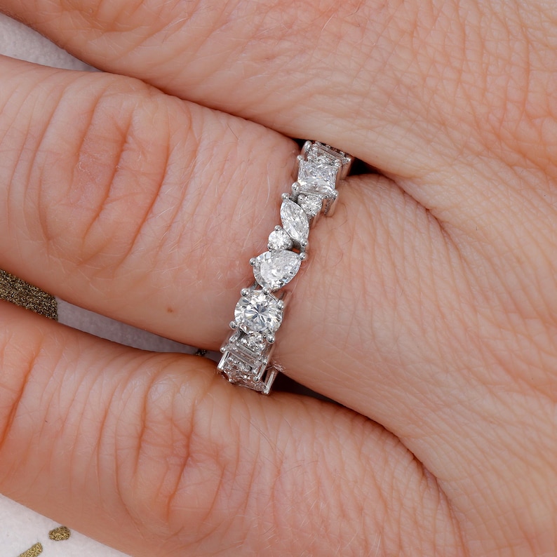 May include: A silver band ring featuring a row of sparkling diamonds in various shapes, including round, pear, and square.