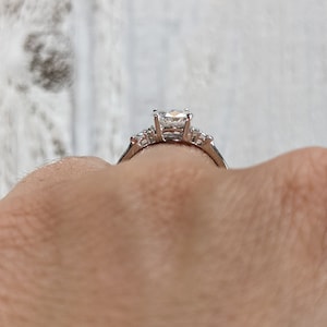 May include: A silver engagement ring with a large, clear, square-shaped center stone and smaller accent stones on the band.