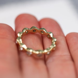 May include: A gold band ring with a scalloped edge and small clear stones set in the band.