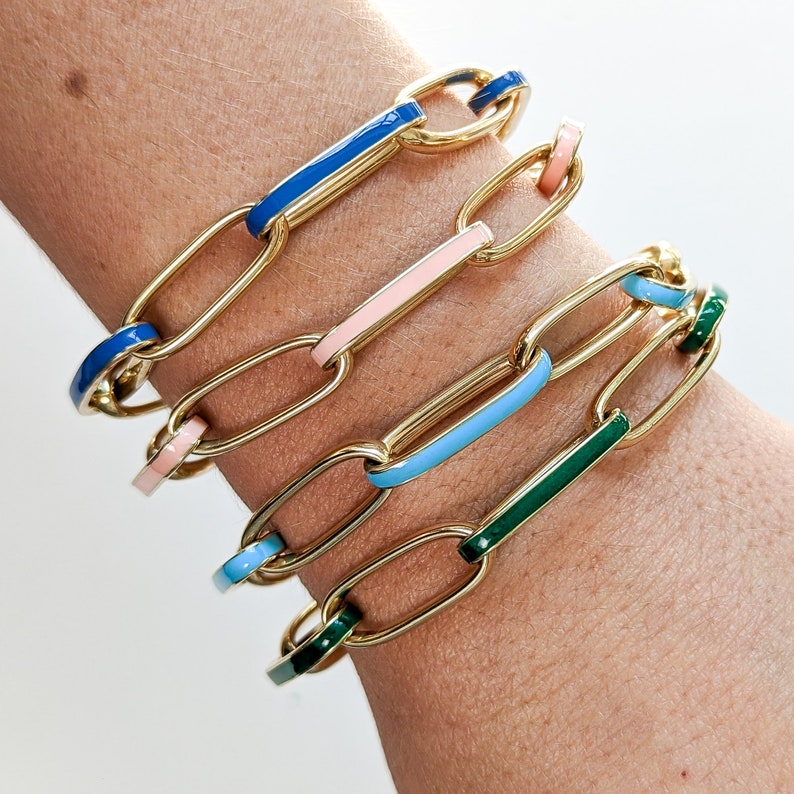 Peut inclure: Quatre bracelets en cha&icirc;ne dor&eacute;e avec des accents en &eacute;mail color&eacute;. Les bracelets sont empil&eacute;s sur le poignet d'une personne. Les couleurs de l'&eacute;mail sont le bleu, le rose, le bleu clair et le vert.