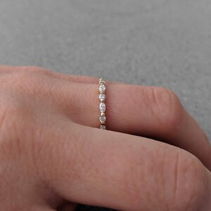 May include: A delicate gold band ring with a row of small, clear, oval-shaped gemstones.