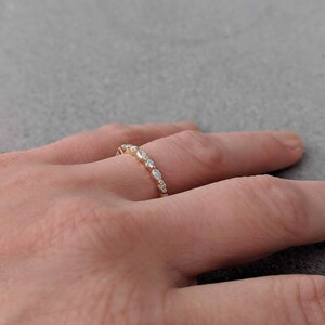 May include: A delicate gold band with a row of small, clear, oval-shaped stones.