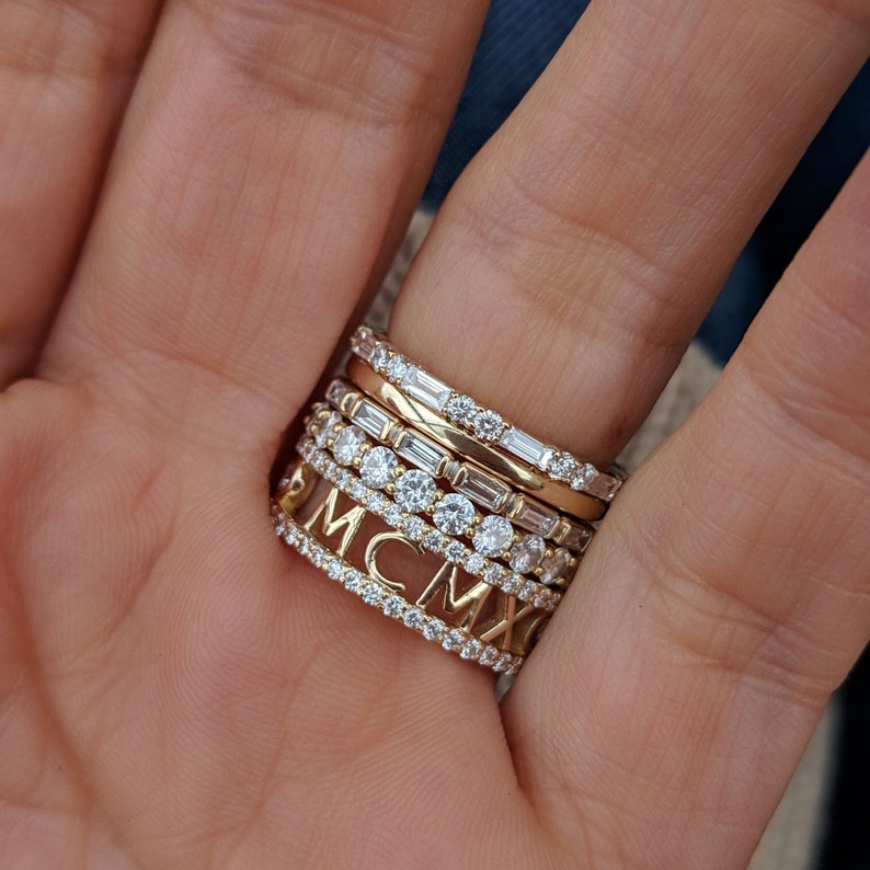 May include: A stack of gold rings with small diamonds. The bottom ring has the letters MCMXV engraved on it.
