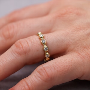 May include: A gold band ring with a row of bezel-set round diamonds.