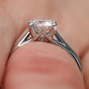 May include: Close-up of a silver engagement ring with a large, clear diamond. The ring has a classic solitaire design with a four-prong setting, showcasing the diamond's brilliance. The band is smooth and polished.