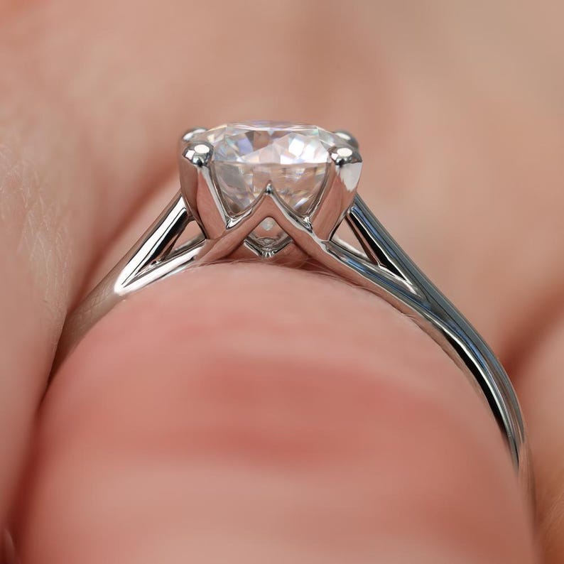 May include: Close-up of a silver engagement ring with a large, clear diamond. The ring has a classic solitaire design with a four-prong setting, showcasing the diamond's brilliance. The band is smooth and polished.