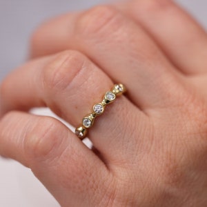May include: A gold band ring with a row of bezel-set round diamonds.