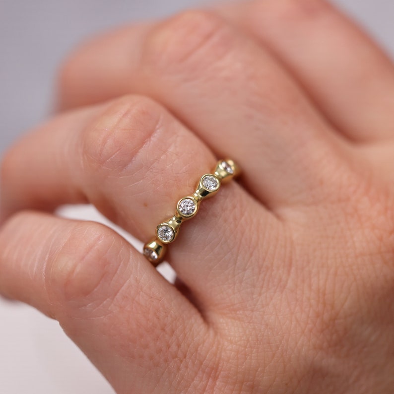 May include: A gold band ring with a row of bezel-set round diamonds.