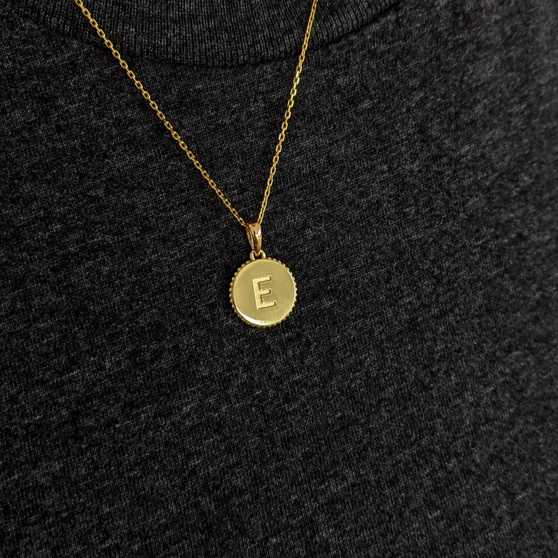 May include: A gold chain necklace with a round pendant featuring the letter "E" in a gold finish.