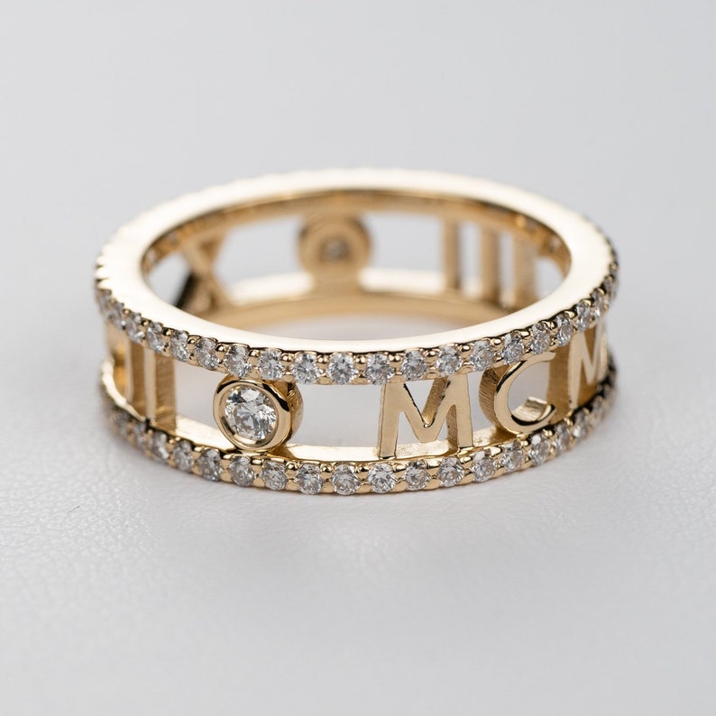 May include: A gold ring with a double row of small diamonds and the letters MCM in the centre. The ring also has Roman numerals on the sides.