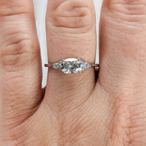 May include: A silver ring with a large oval-shaped center stone and two smaller round stones on either side.